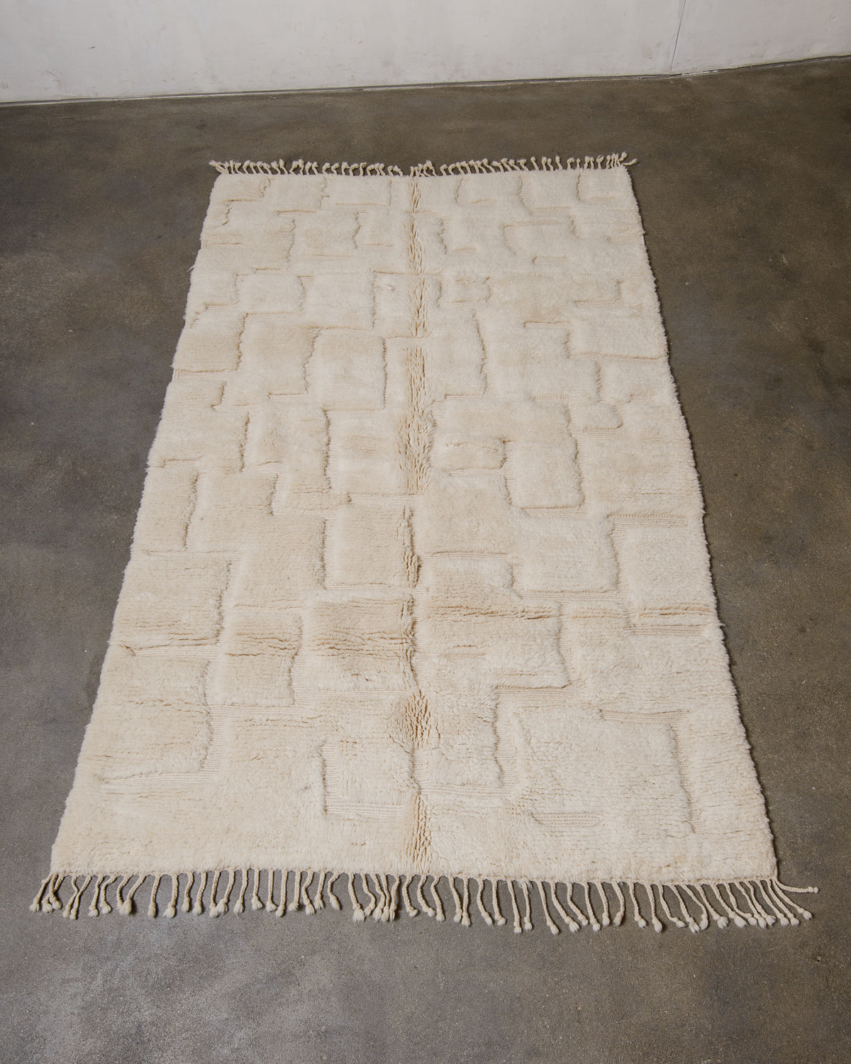 Cream woven rug with fringes on a concrete floor